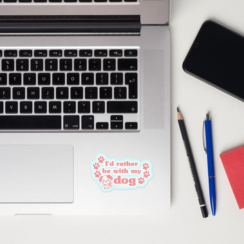 Laptop with a sticker saying 'I'd rather be with my dog' on a white surface with a phone, pencil, and pen.