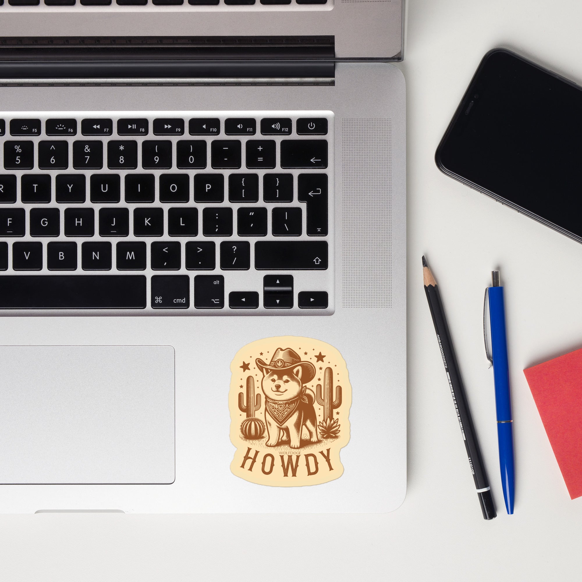 Laptop with a 'Howdy' sticker, phone, and pens on a white surface