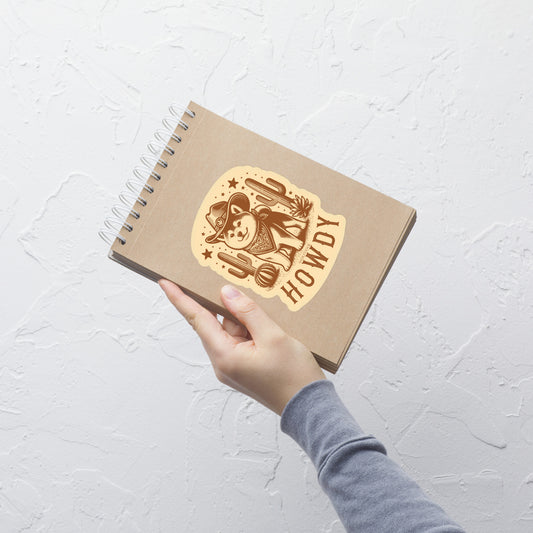 Hand holding a brown notebook with 'Howdy' design on a light gray background